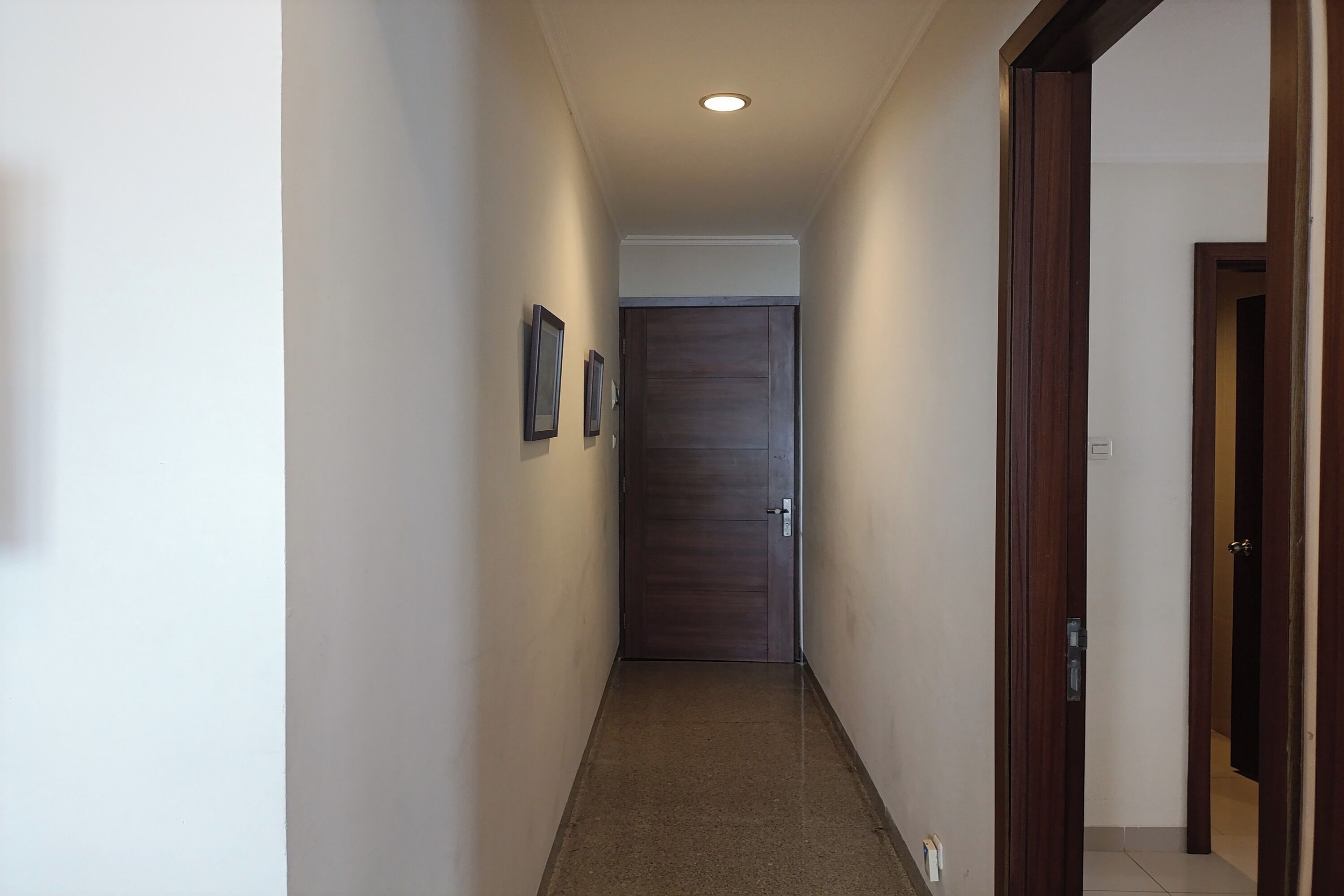 A narrow hallway with a wooden door at the end, white walls, and a light fixture on the ceiling.