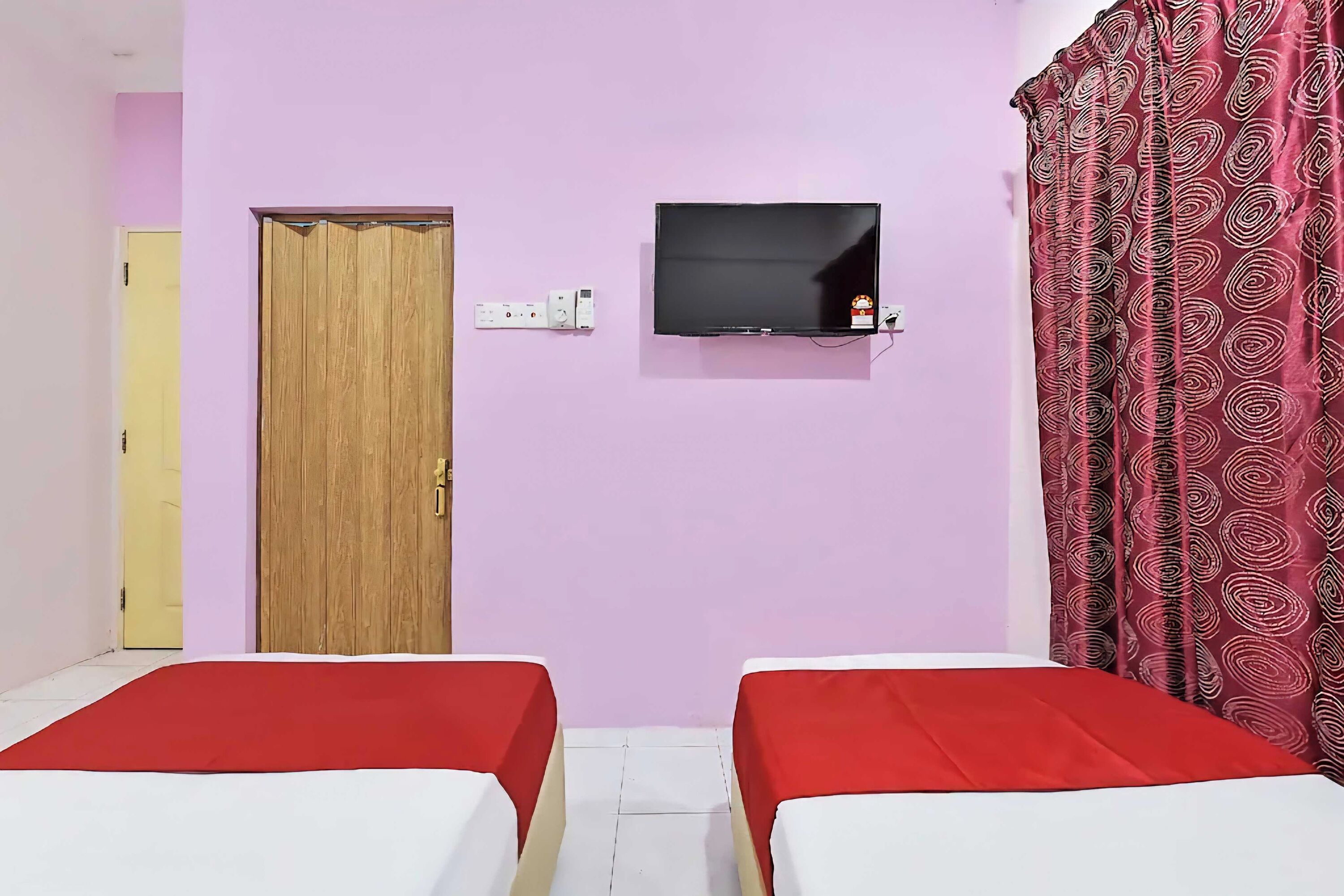 Habitación con dos camas, un televisor montado en la pared, una puerta de madera y una cortina estampada.