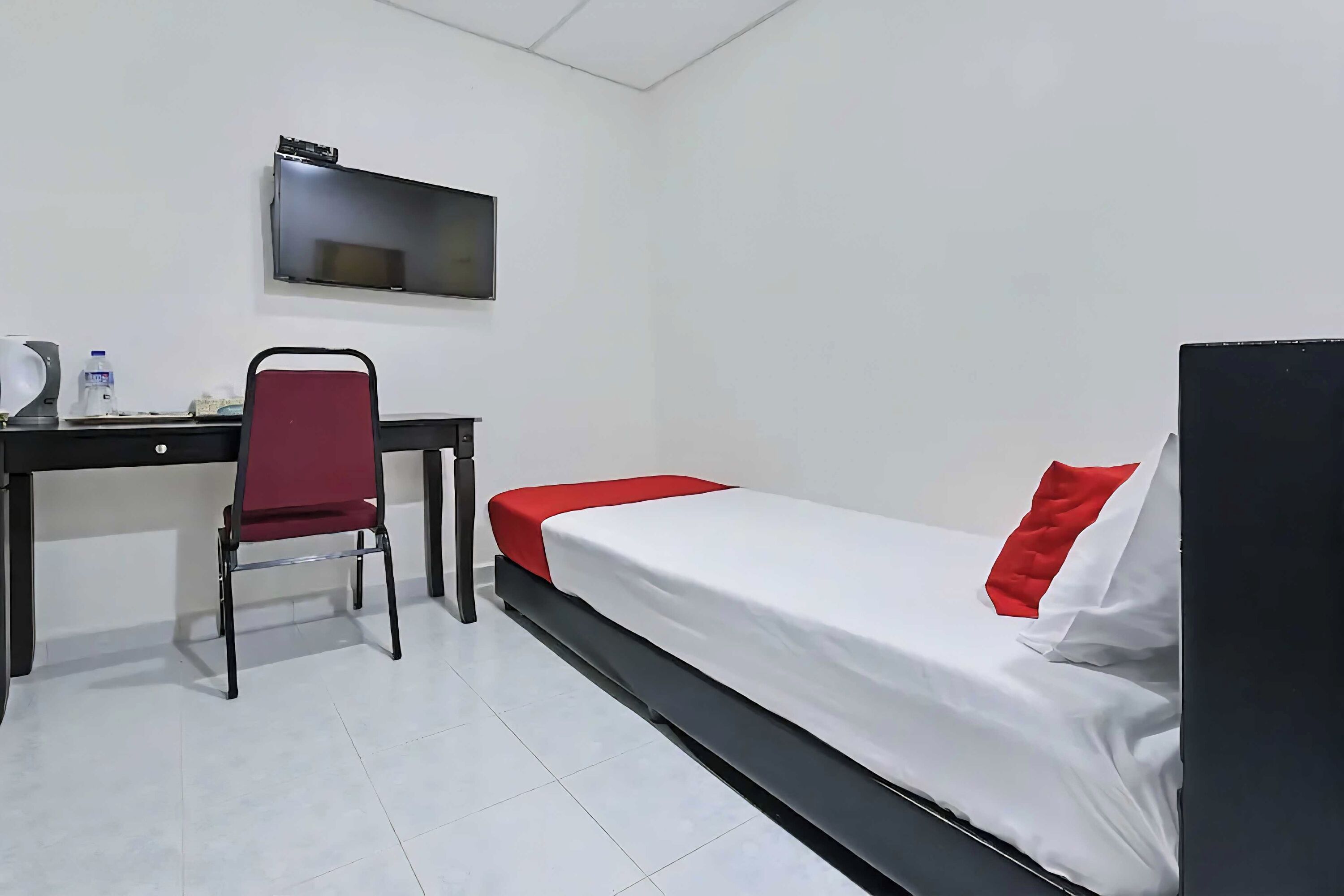 Una habitación con una cama, un escritorio, una silla, un televisor de pantalla plana y una botella de agua.