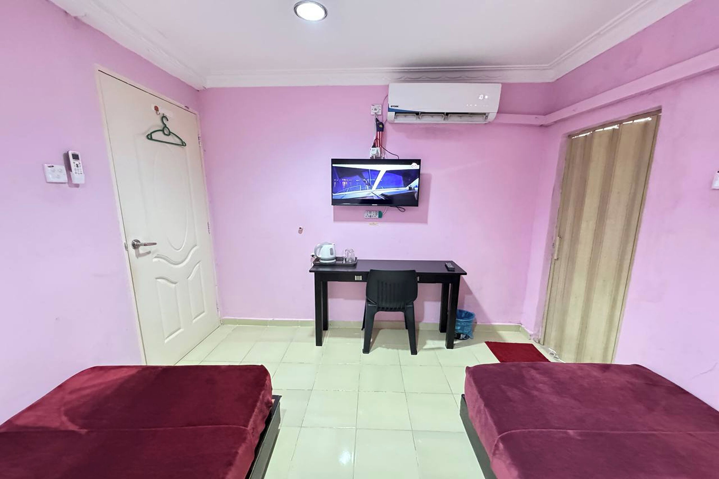 A room with pink walls, a bed, a desk with a chair, a TV, and an air conditioner.