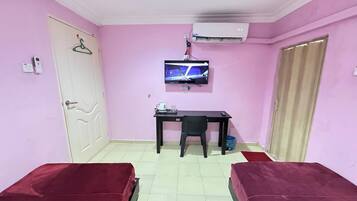 A room with pink walls, a bed, a desk with a chair, a TV, and an air conditioner.