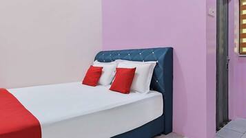 Una cama con una colcha blanca y roja, un cabecero tapizado en azul y dos almohadas rojas.