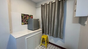 A small bathroom with a toilet, a sink, a mirror, a shower curtain, and a refrigerator. - Sukhum Suvarnabhumi Airport Guest House (Bangkok)