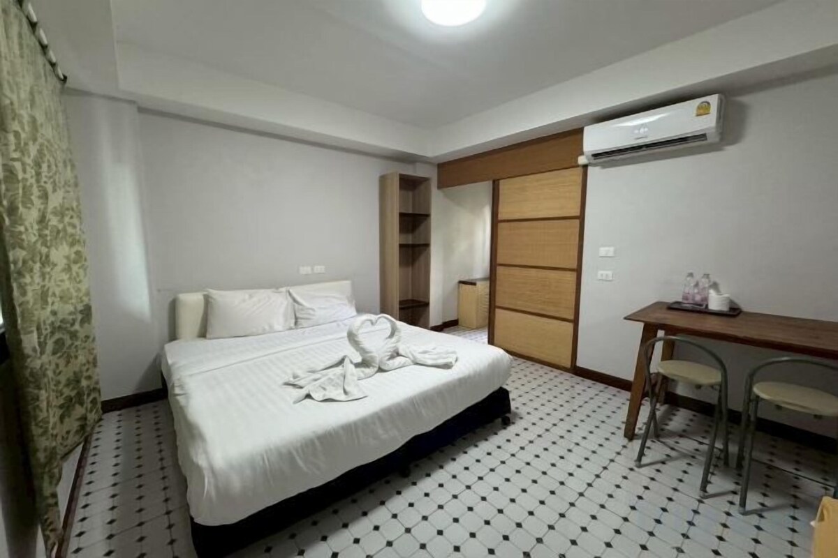 A hotel room with a bed, a desk, and an air conditioning unit.