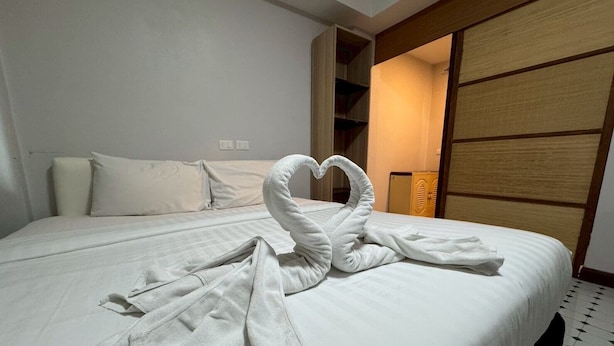 A hotel room with a neatly made bed, a wooden wardrobe, and a wall-mounted shelf. - Sukhum Suvarnabhumi Airport Guest House (Bangkok)
