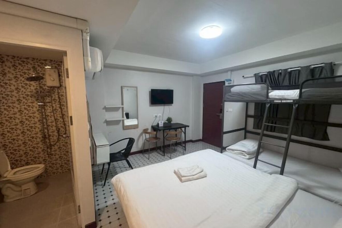 A hotel room with bunk beds, a desk, a chair, a toilet, and a television.