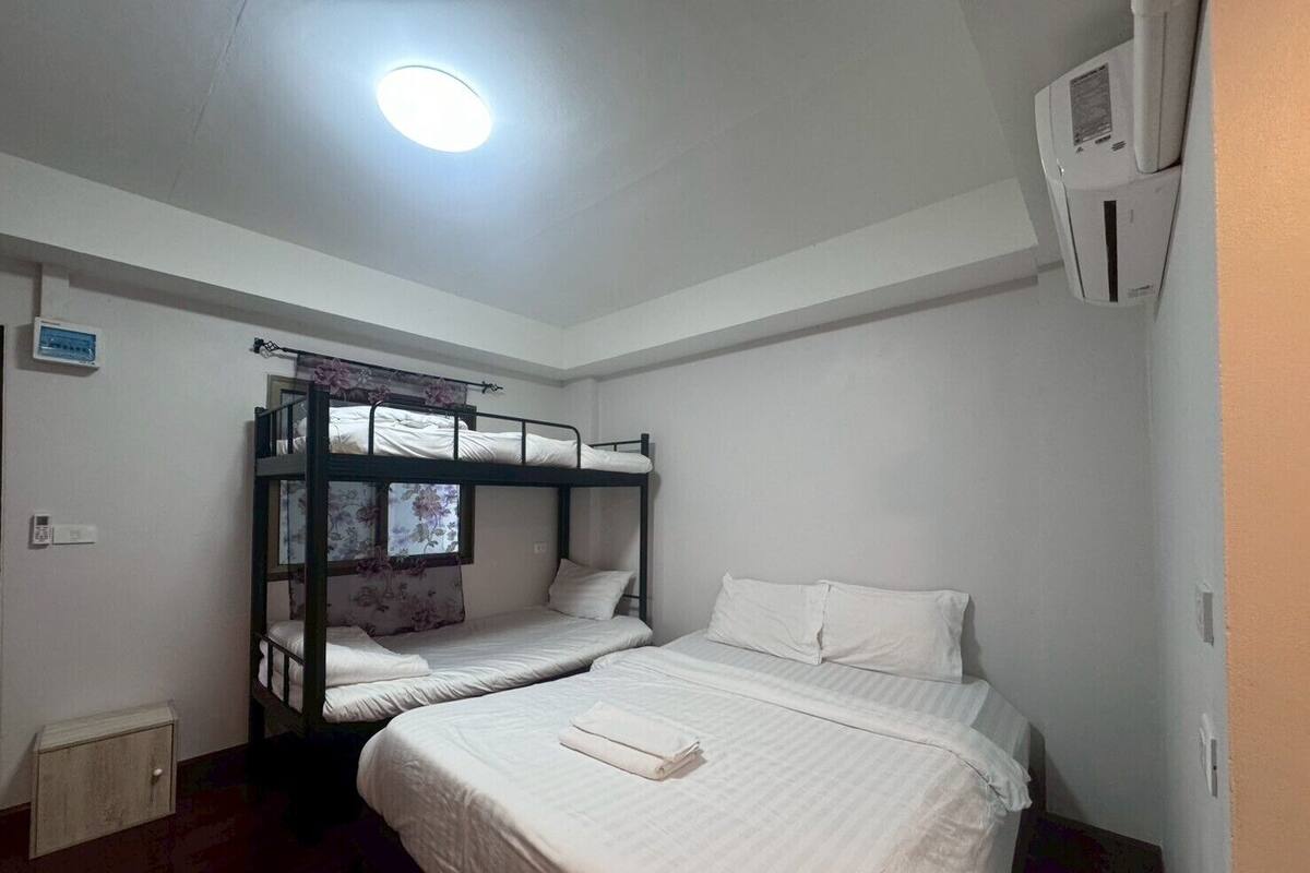 A dormitory room with bunk beds, a small bedside table, and a window with floral curtains.