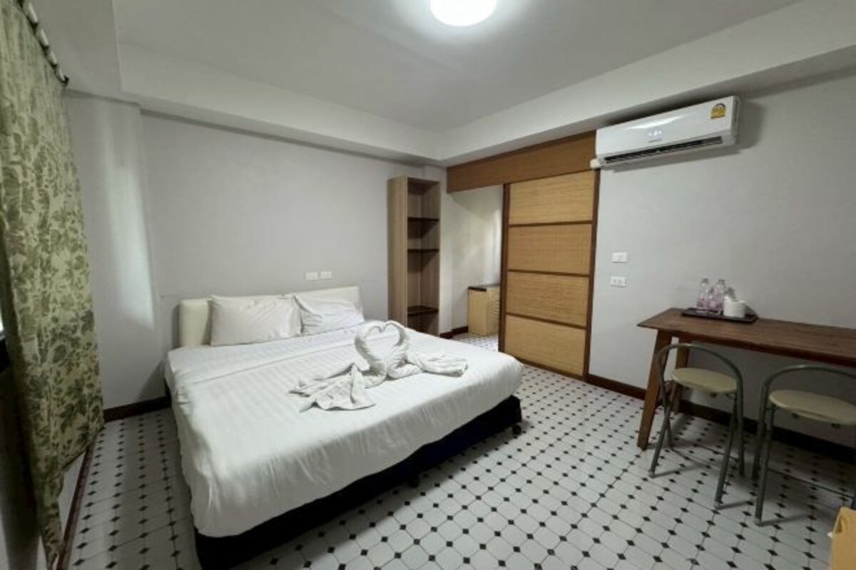 A hotel room with a bed, a desk with two chairs, an air conditioning unit, and a patterned floor.