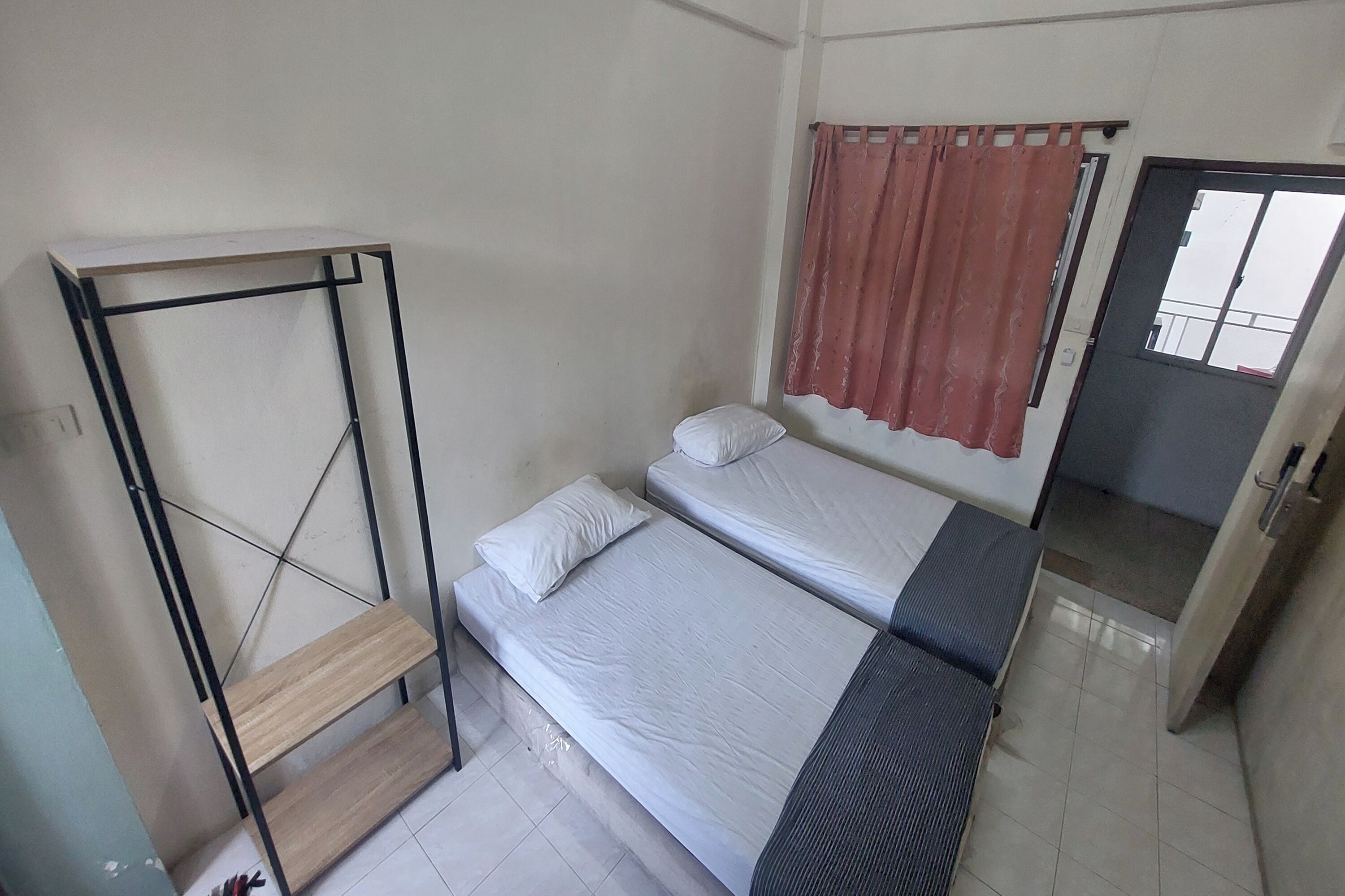 A small, simple room with two single beds, a wooden shelf unit, and a door leading to another room.