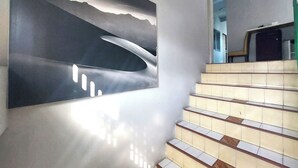 Una escalera de diseño moderno, un cuadro abstracto de gran tamaño en la pared y una vista de un edificio al fondo.