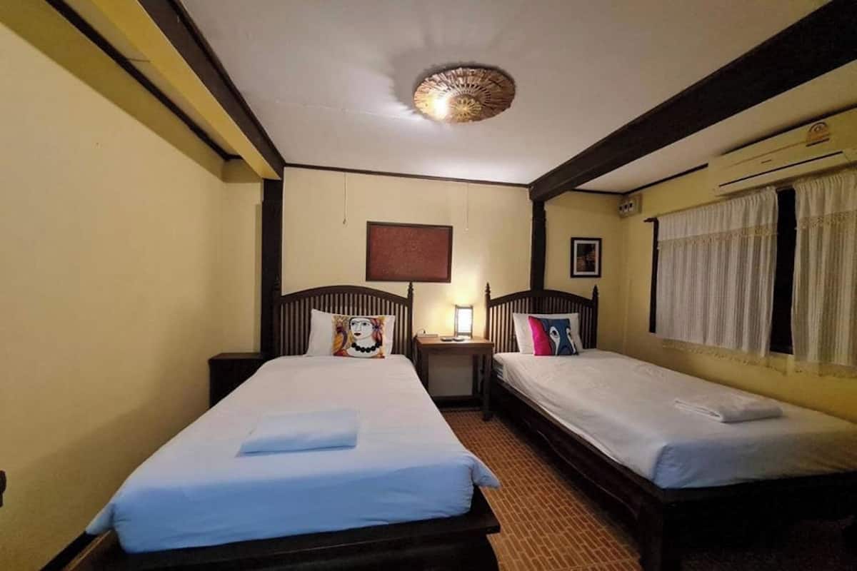 Une chambre d’hôtel avec deux lits simples, une petite table, une lampe fixée au mur et une fenêtre avec des rideaux.