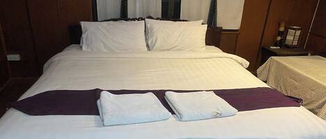 A neatly made bed with white linens and a purple throw blanket, a wooden headboard, and a small bedside table with a lamp.