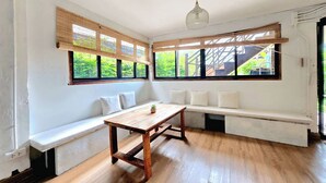 A room with a wooden table, white bench, large windows, and a ceiling light fixture. - Nearthepark Boutique House (Chiang Mai)