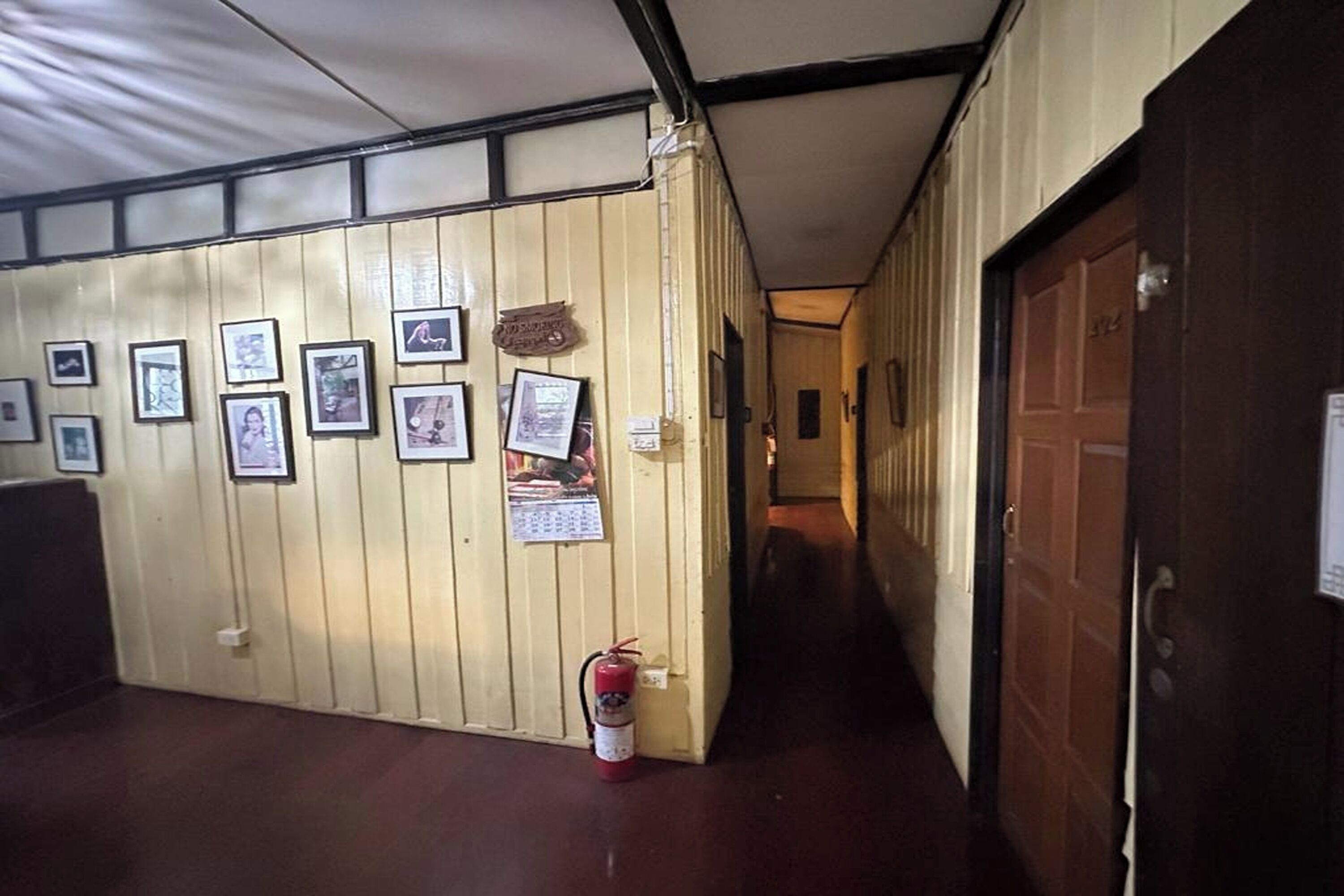 Un corridoio con quadri appesi al muro, un estintore e una porta in legno.