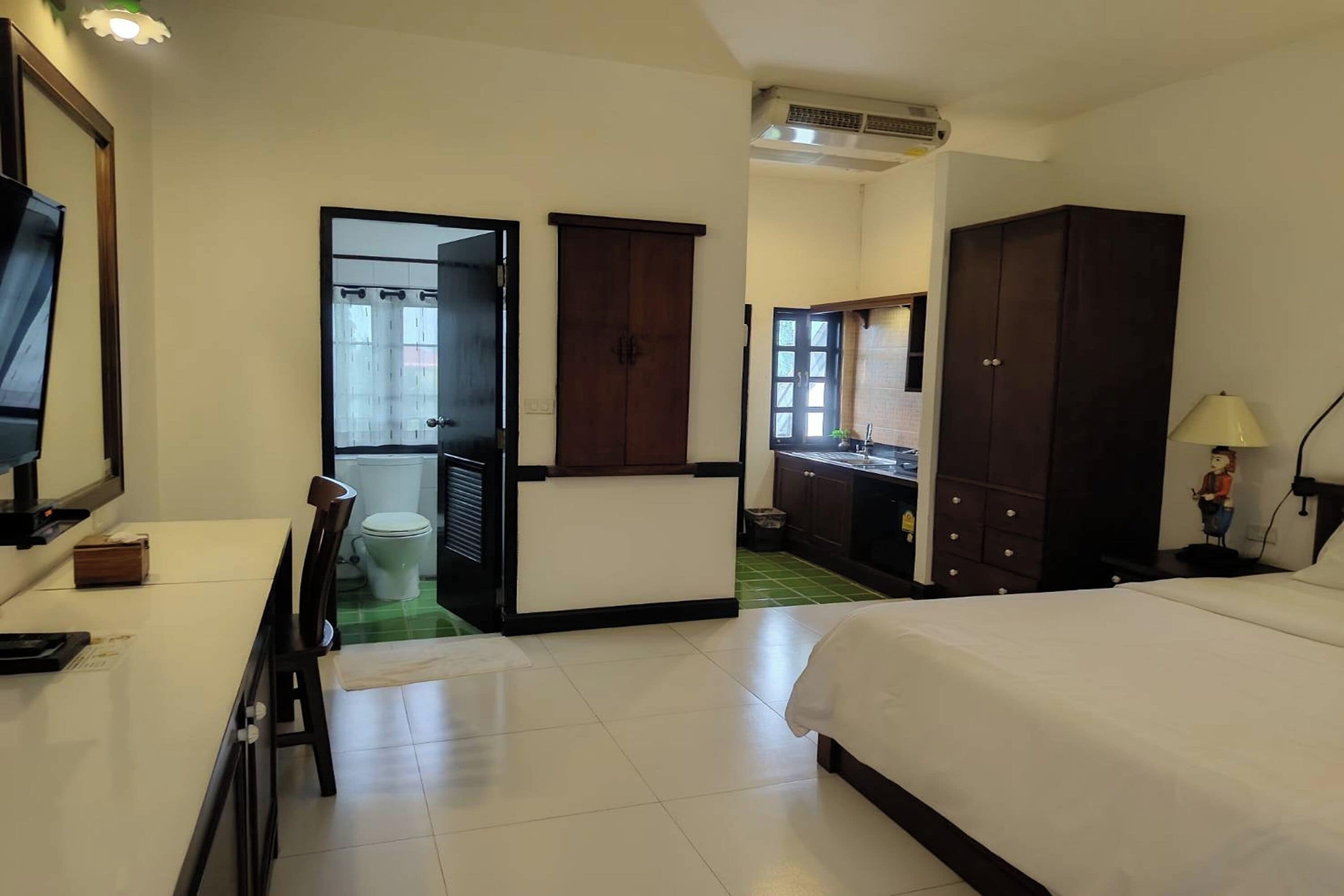 A hotel room with a bed, a desk, a chair, a wardrobe, a bathroom with a toilet, and a mirror.