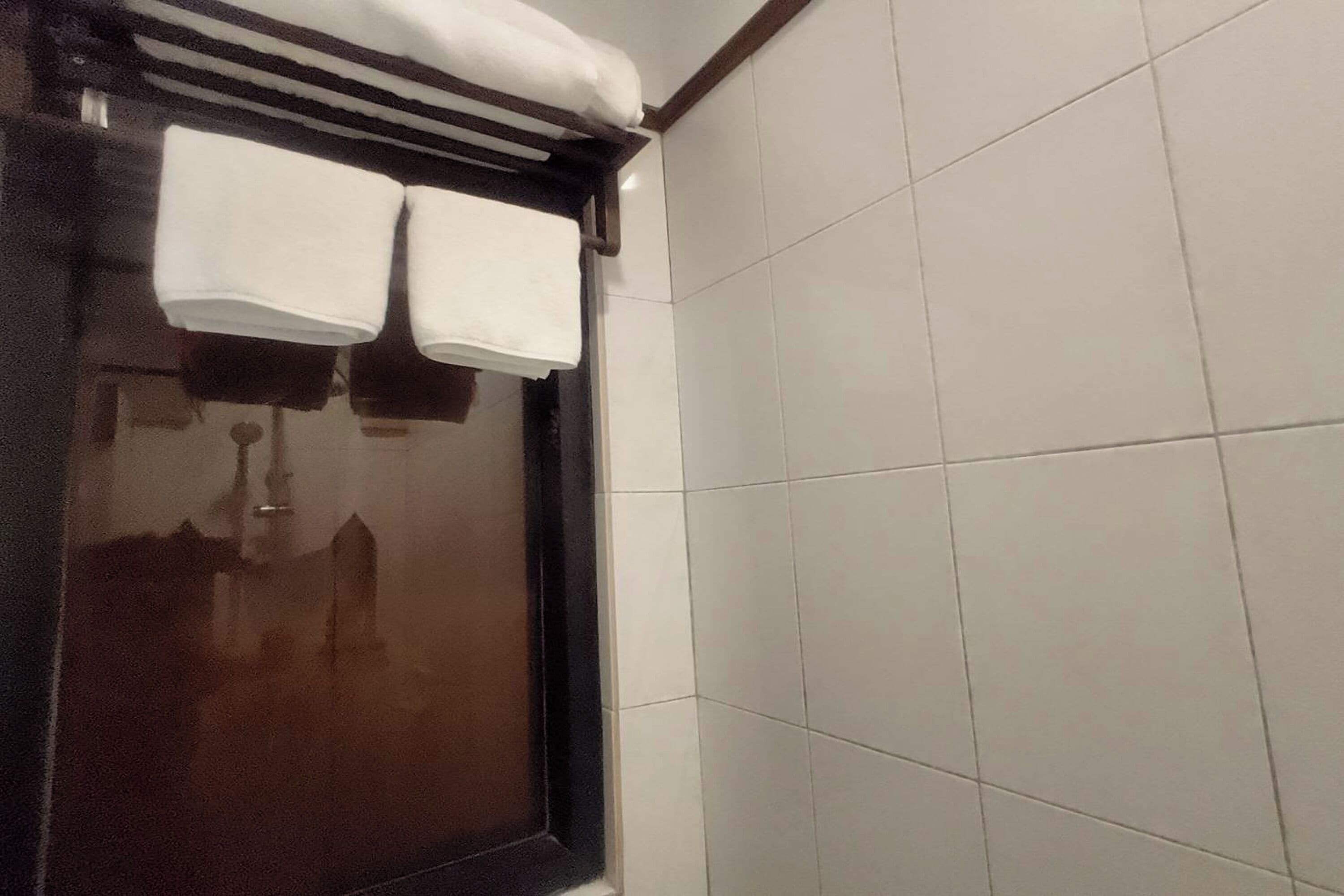 A bathroom with white tiled walls, a window with a towel rack, and a visible reflection of a building outside.