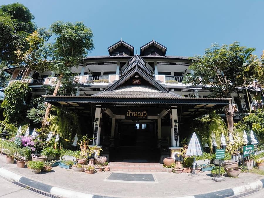 Un bâtiment traditionnel avec une entrée centrale, entouré de plantes en pot et sous un ciel dégagé.