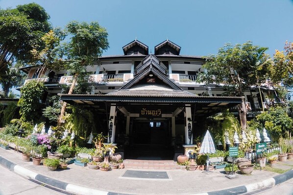 A traditional building with a central entrance, surrounded by potted plants and a clear sky.