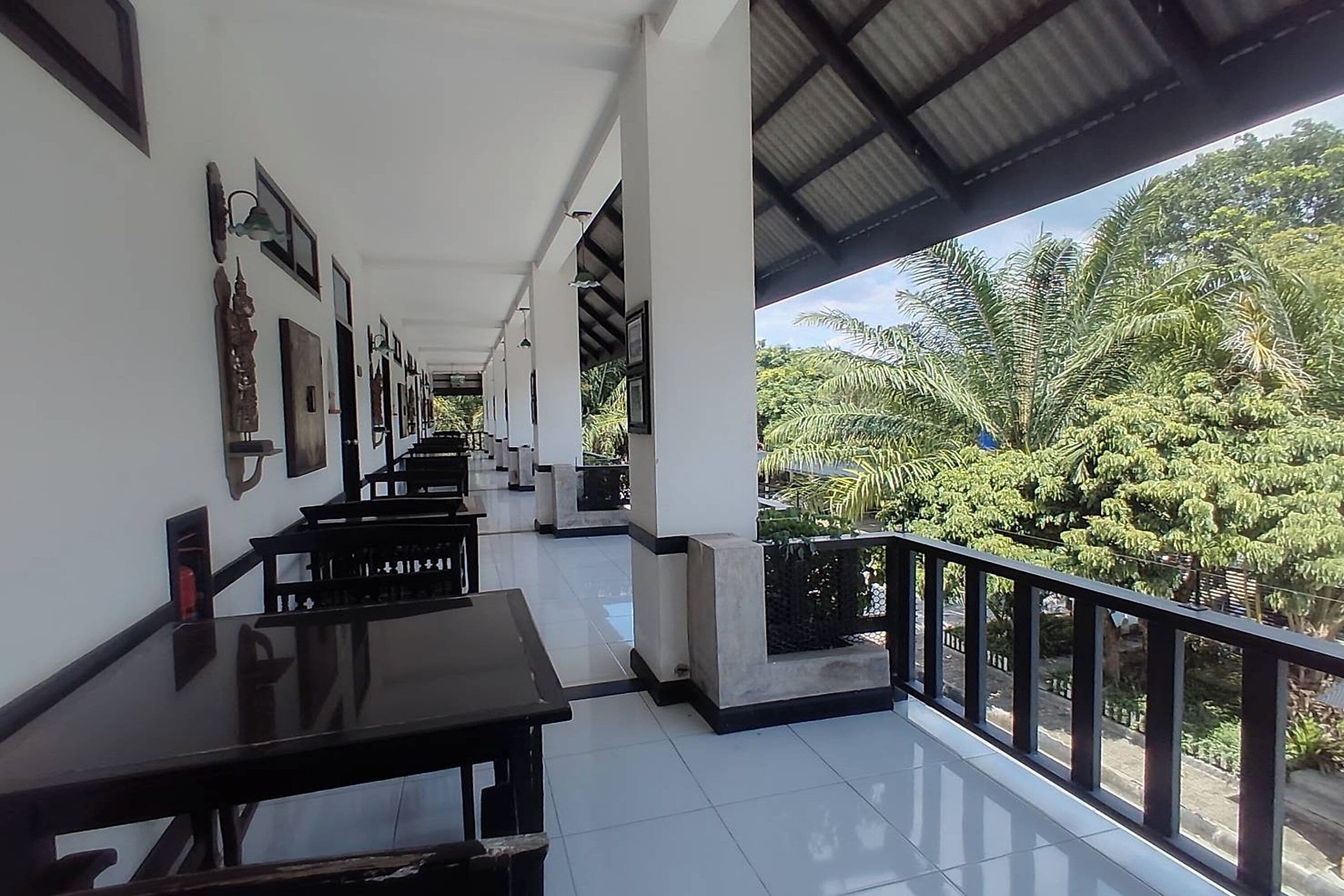 A covered outdoor area with tables and chairs, a railing, and a view of greenery.