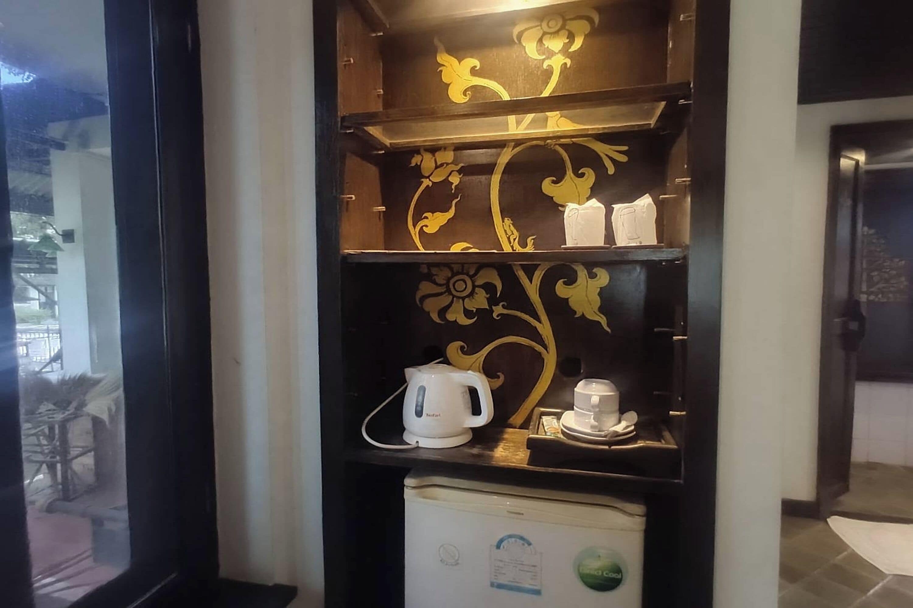 A room with a coffee machine and a refrigerator on a shelf.