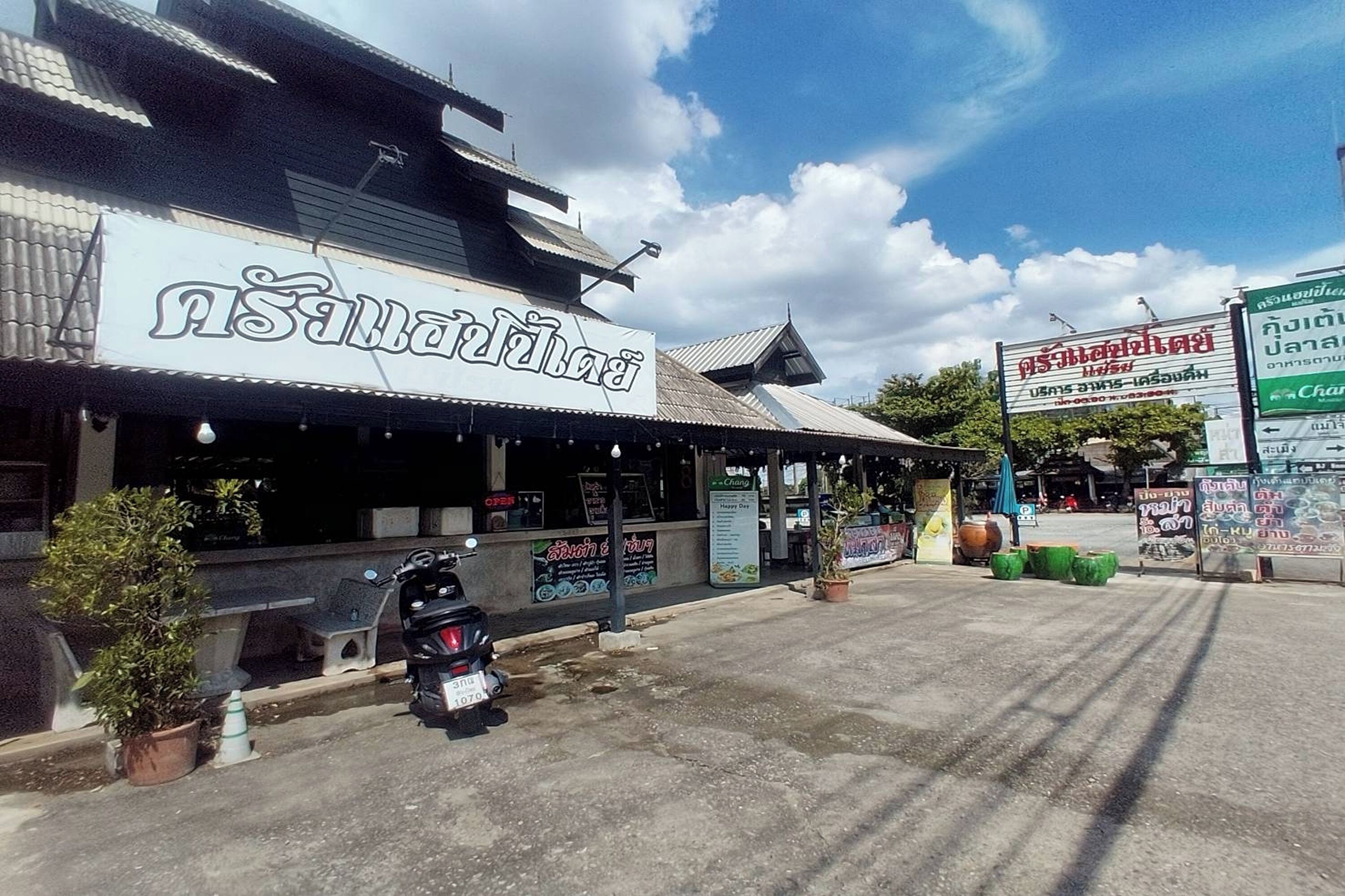 A restaurant with a sign in a foreign language, outdoor seating, and a motorcycle parked in front.