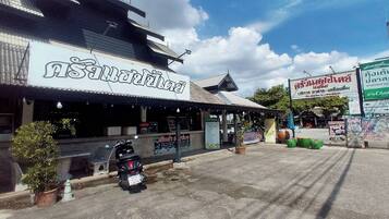 A restaurant with a sign in a foreign language, outdoor seating, and a motorcycle parked in front.