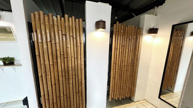 Une pièce avec des cloisons en bambou, un grand miroir et une petite plante posée sur une étagère.