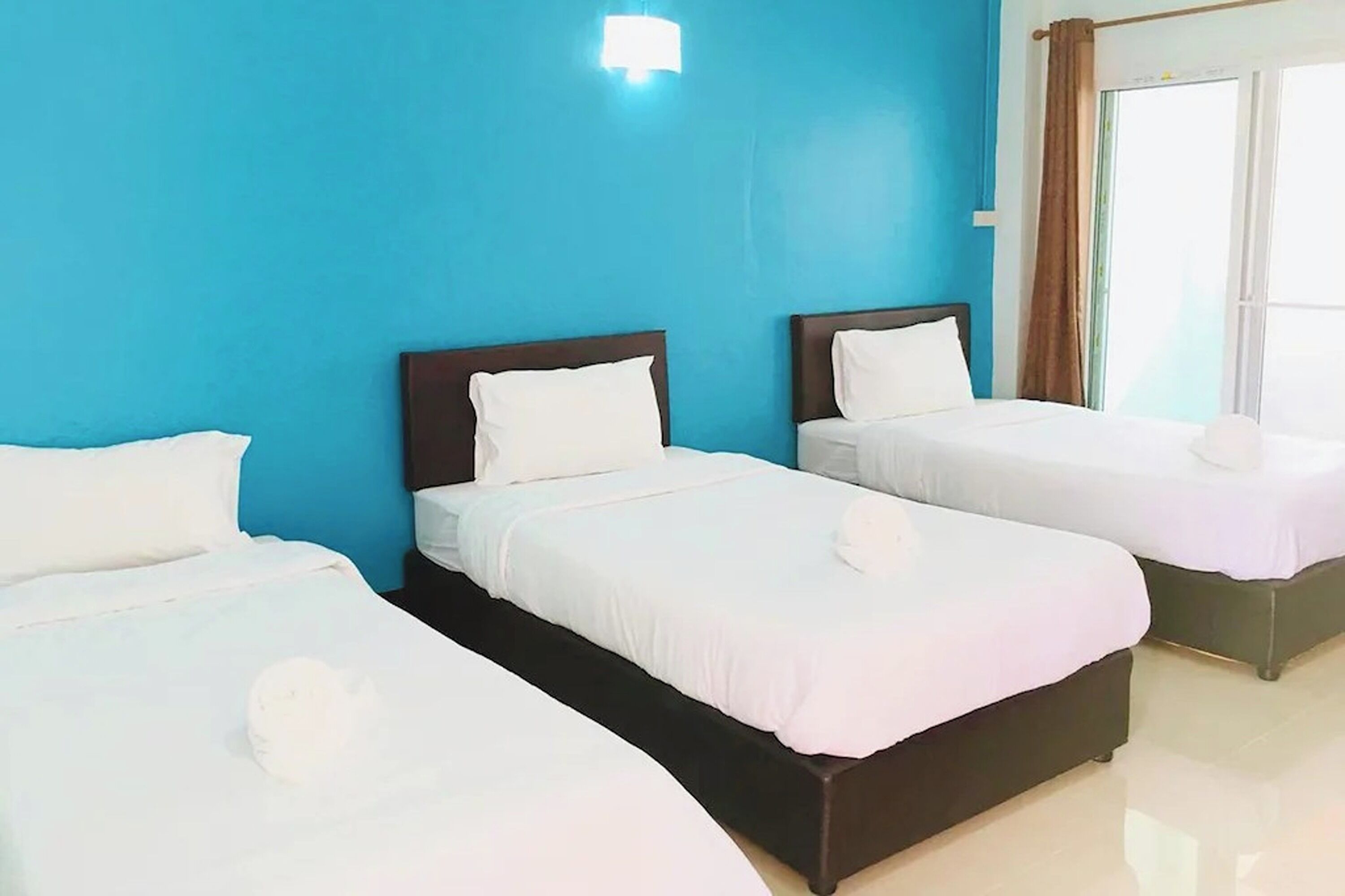 A hotel room with two beds, each with white bedding and pillows, against a blue wall.