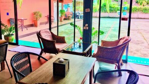 Un café con sillas de mimbre y una mesa de madera, ventanas amplias con vistas a un jardín y motocicletas estacionadas.