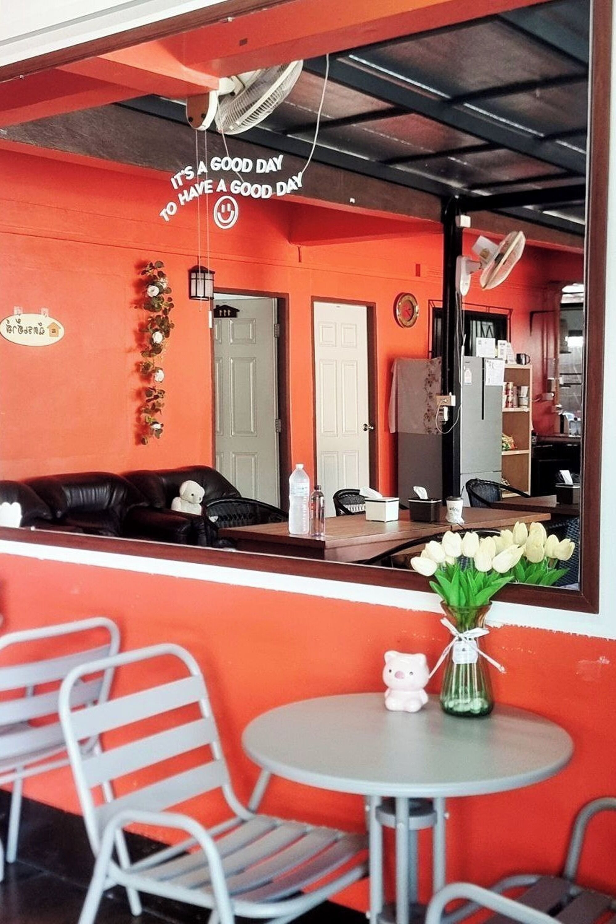 Ein Zimmer mit roter Wand, einem schwarzen Ledersofa, einem kleinen runden Tisch mit Blumenvase und einem Spiegel, der das Zimmer widerspiegelt.