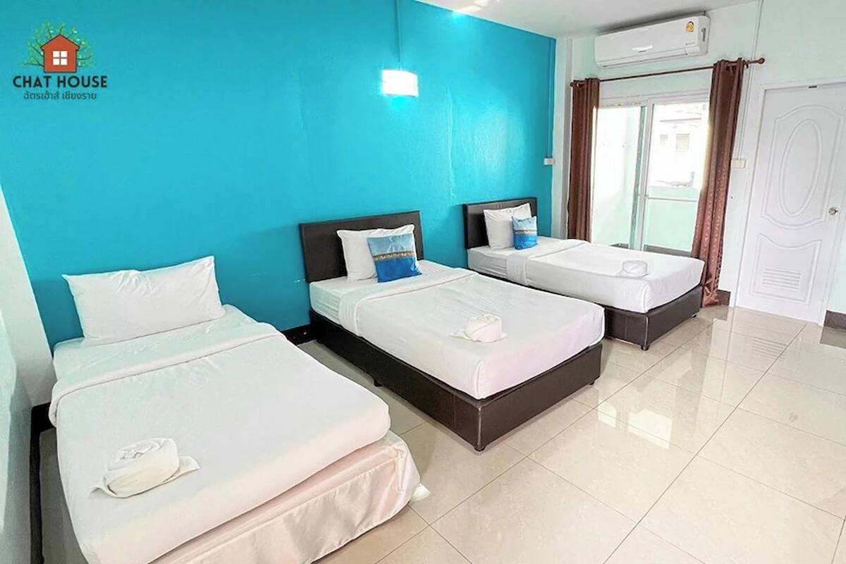 A hotel room with three beds, a blue wall, a white door, and an air conditioning unit.