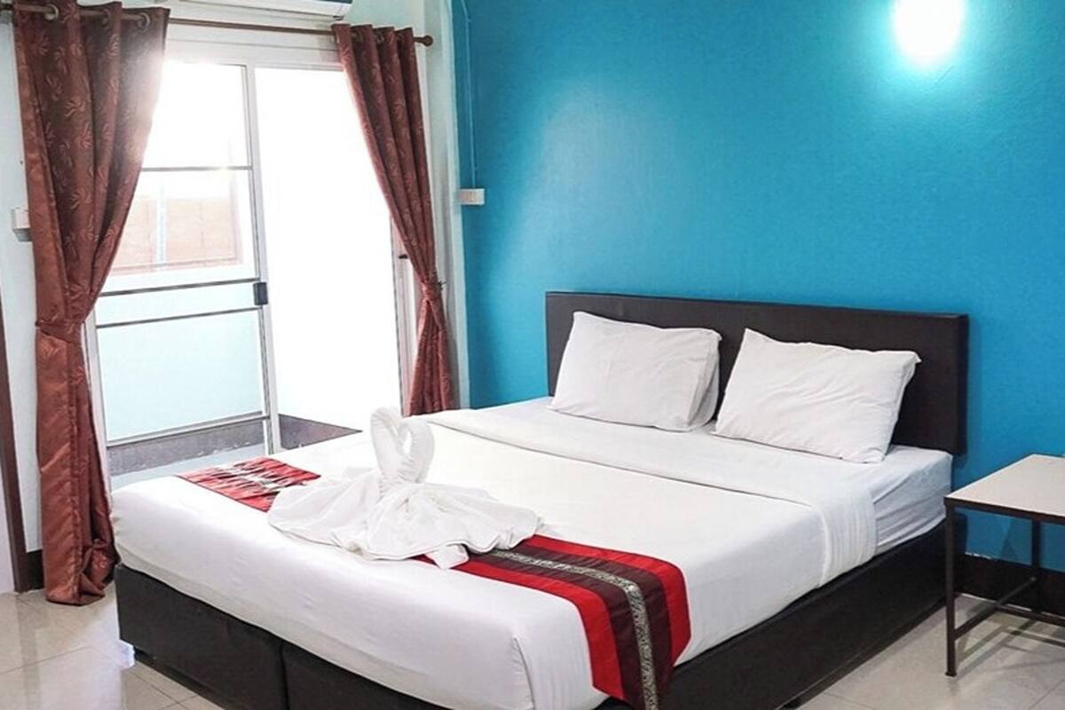 A hotel room with a bed, a window with curtains, and a blue wall.