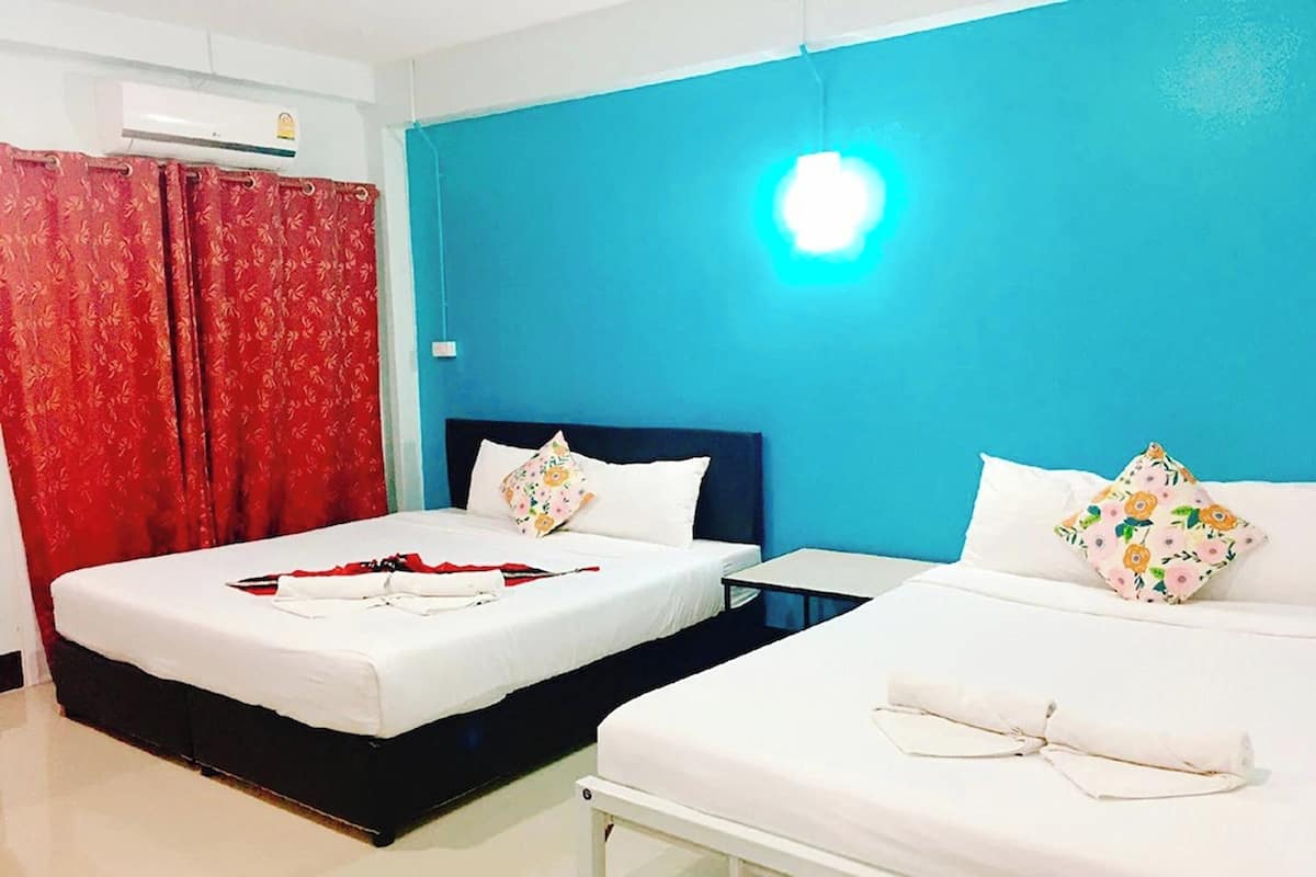 A hotel room with two beds, a red curtain, a blue wall, and a white air conditioning unit.