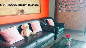 Un sofá de cuero negro con almohadas rosadas y un oso de peluche, una mesa de centro de madera con una planta en maceta, y una pared con cuadros enmarcados.