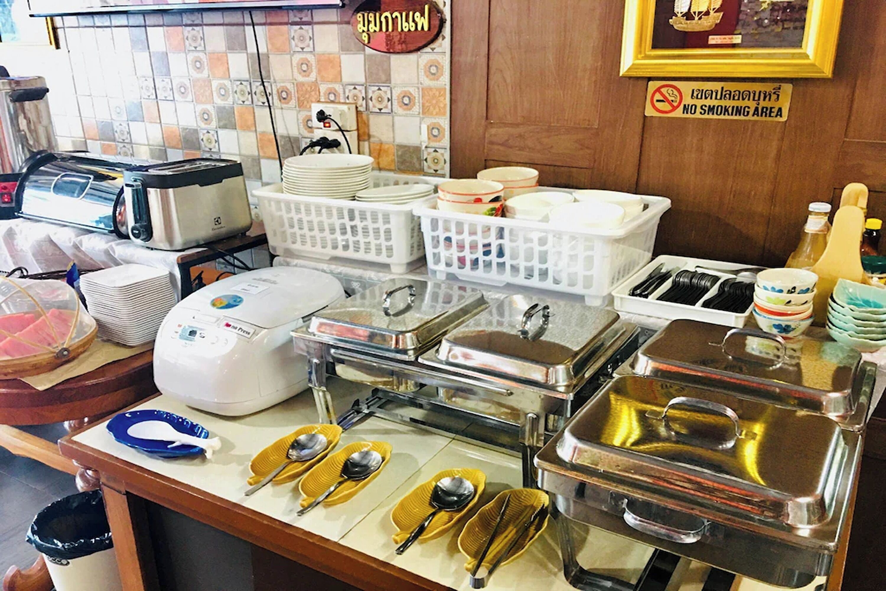 Montaje de bufé con varios recipientes de comida, utensilios para servir y un cartel de prohibición de fumar.
