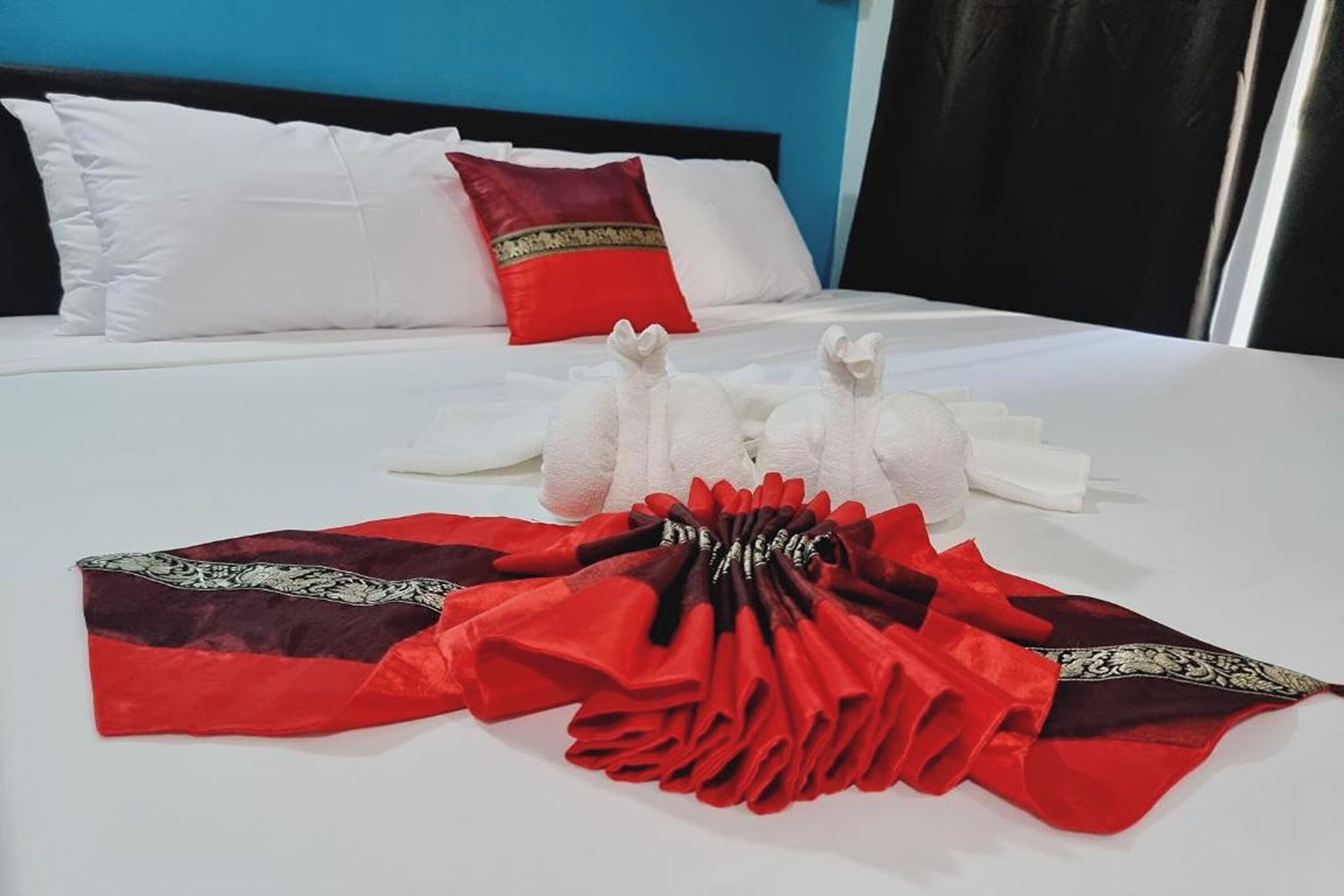 A neatly made bed with white and red pillows, a red and black blanket, and a white towel arrangement.