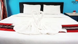 Habitación de hotel con una cama, almohadas blancas, una manta a rayas rojas y negras, y una presentación de toallas con forma de corazón.