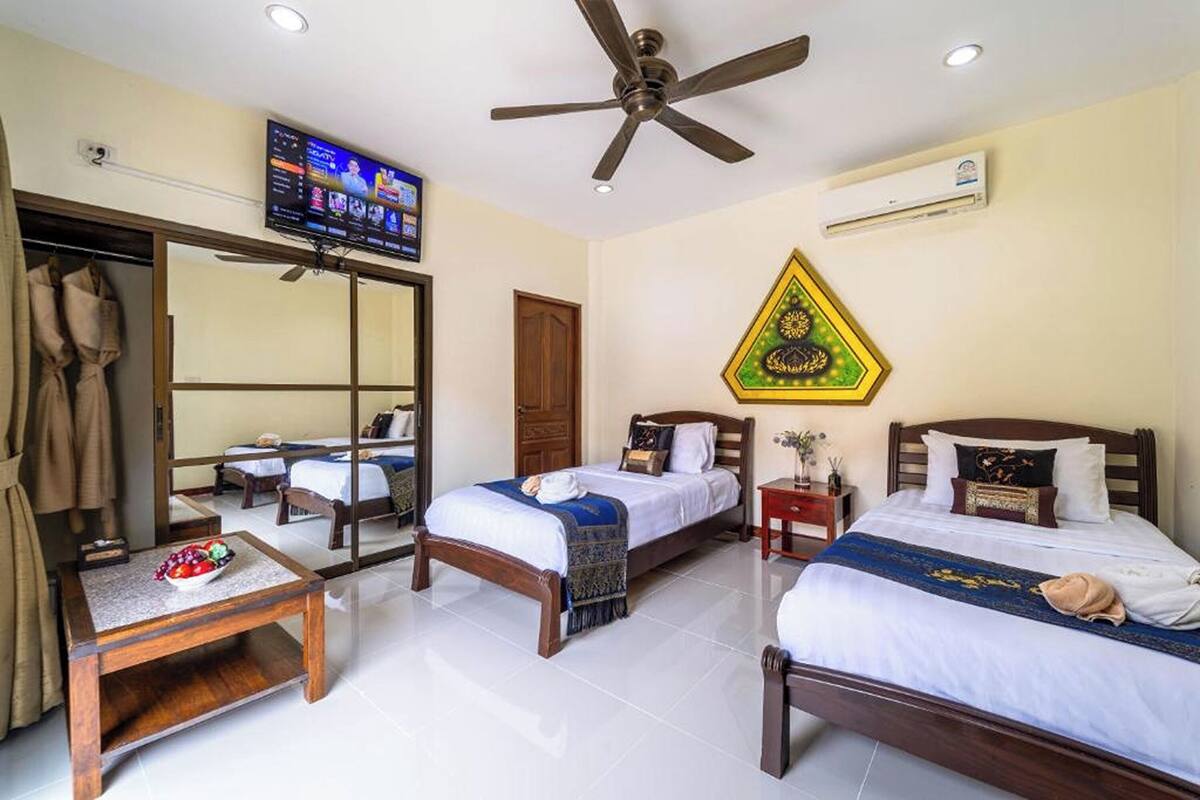 Een hotelkamer met twee bedden, een televisie, een plafondventilator, een airconditioner en een spiegel.
