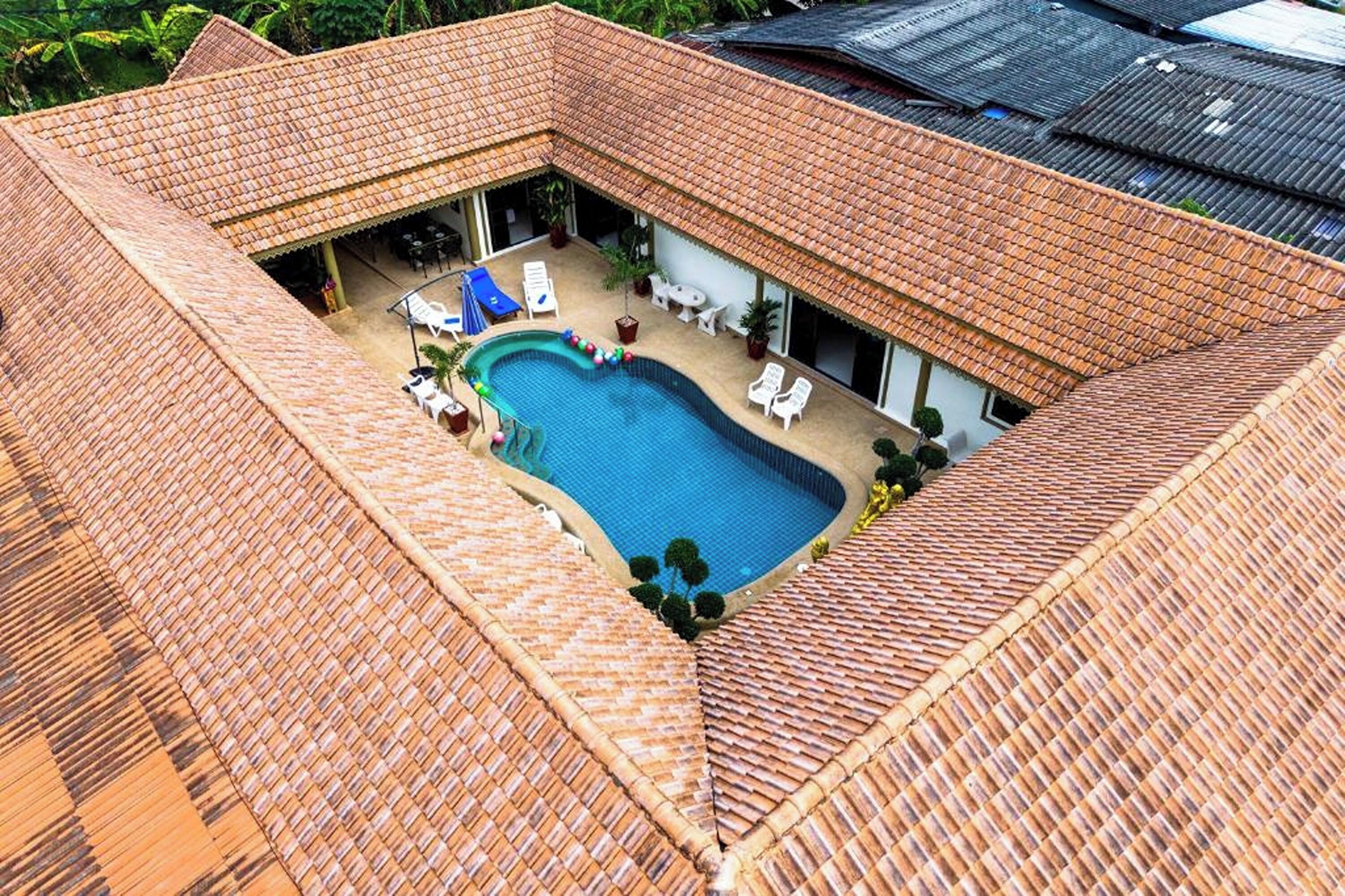 Una piscina en la azotea con techo de azulejos, rodeada de sillas de descanso y un área de estar techada.
