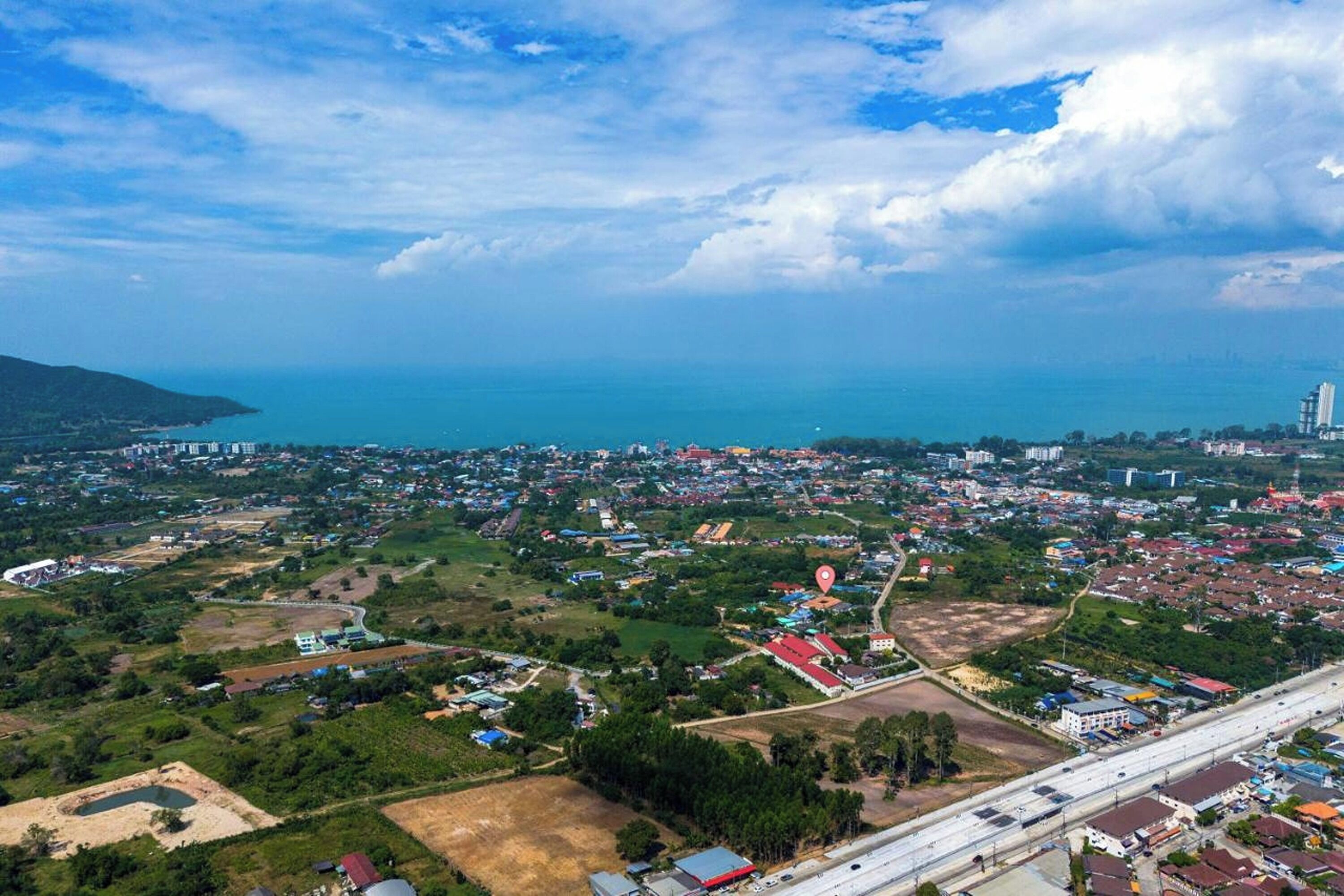An aerial view of a coastal town with a mix of residential and commercial buildings, a highway, and a large body of water.