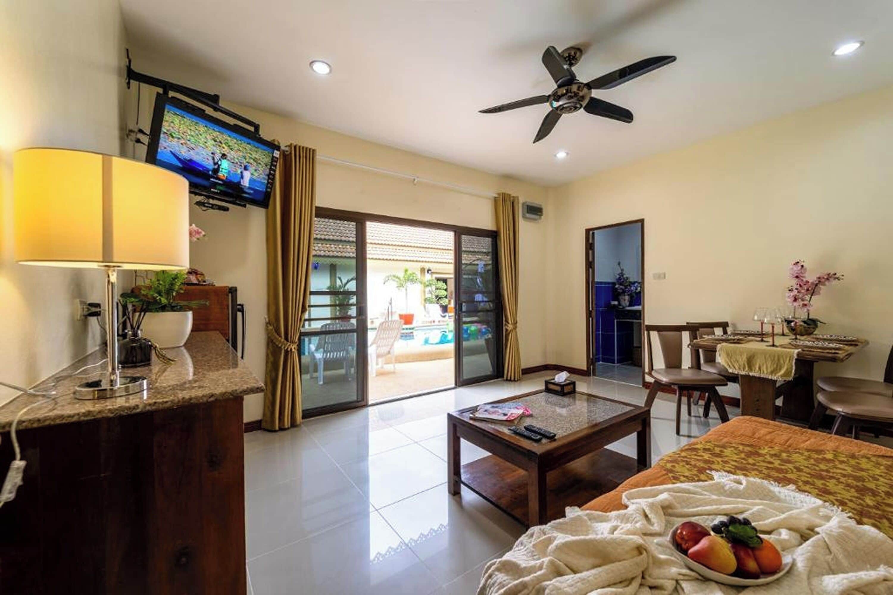 A hotel room with a TV, a ceiling fan, a dining area, and a view of the outside.