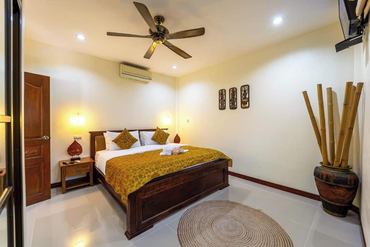 Slaapkamer met een bed, een plafondventilator, een nachtkastje, een wandairconditioner en een potplant.