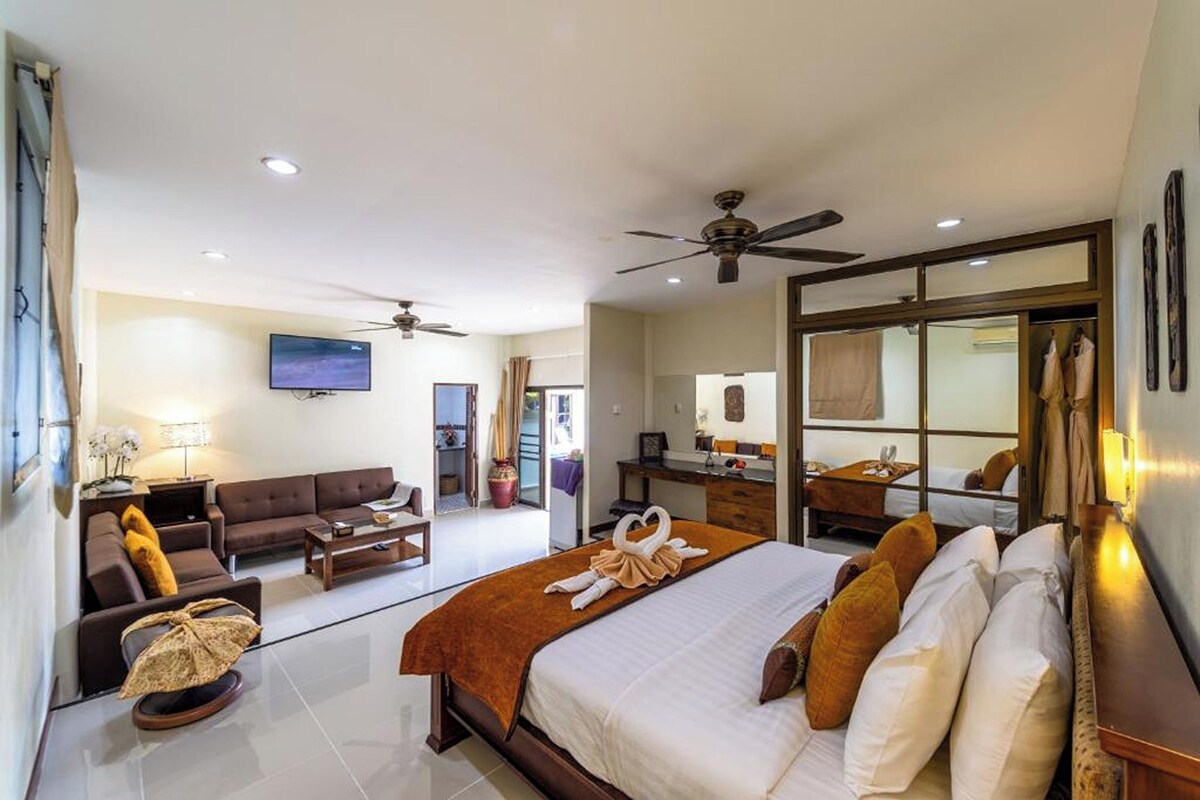 A spacious hotel room with a large bed, a sofa, a desk, and a TV.