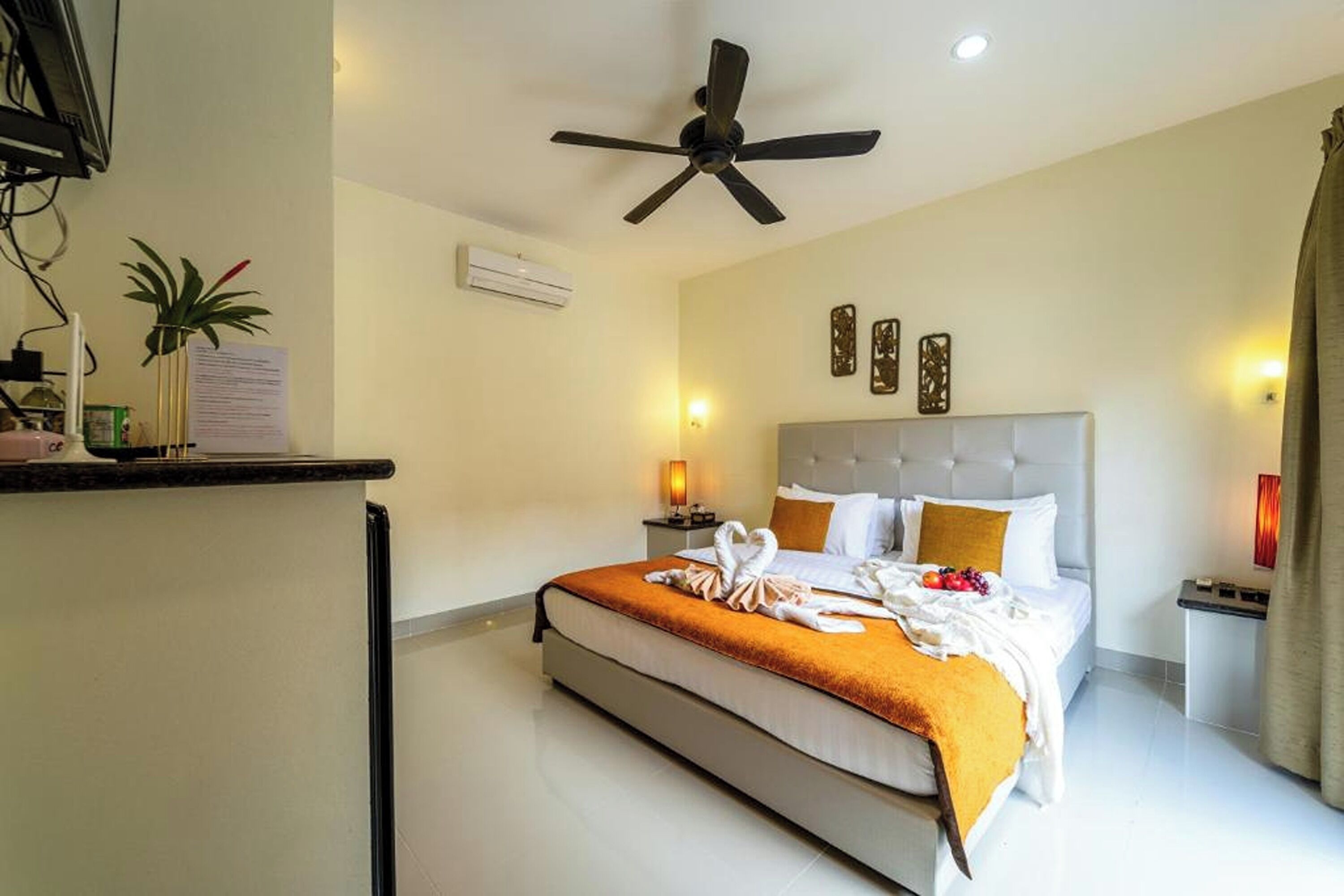 Une chambre d’hôtel équipée d’un lit, d’un ventilateur de plafond, d’une table de chevet, d’une lampe et d’un climatiseur fixé au mur.