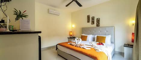 Una habitación de hotel con cama, ventilador de techo, mesita de noche, lámpara y aire acondicionado instalado en la pared.