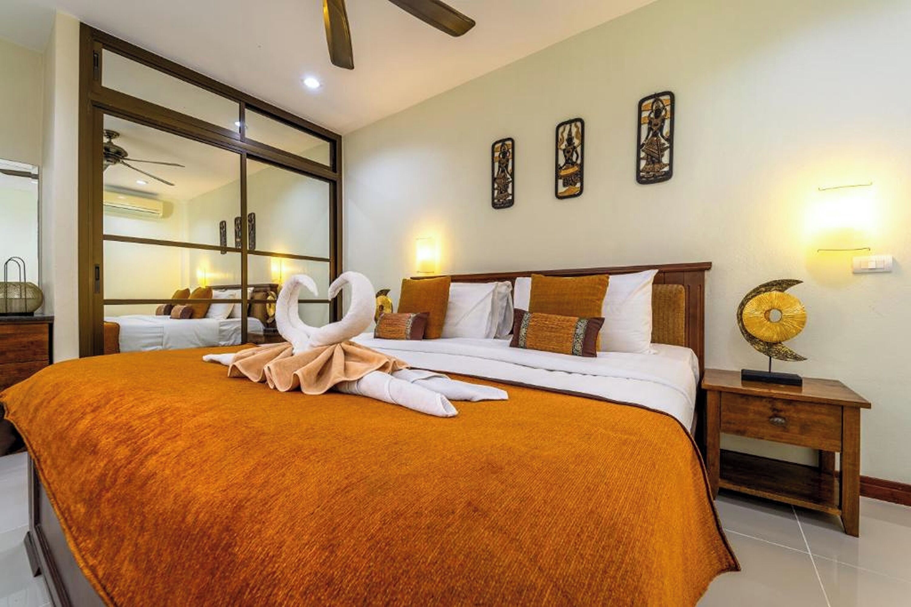 A hotel room with a large bed, a wooden nightstand, a wall-mounted lamp, and a ceiling fan.