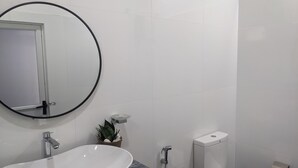 A bathroom with a white sink, a mirror with a black frame, a toilet, and a small plant. - Cealora Resort (Dambulla)