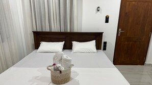 A neatly made bed with white linens, a woven basket with towels, and a wooden headboard. - Cealora Resort (Dambulla)