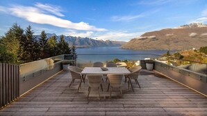 A terrace with a table and chairs overlooking a lake and mountains.