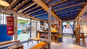Un restaurante con vistas a barcos, mesas de madera y un estandarte rojo que anuncia tours hop-on hop-off.
